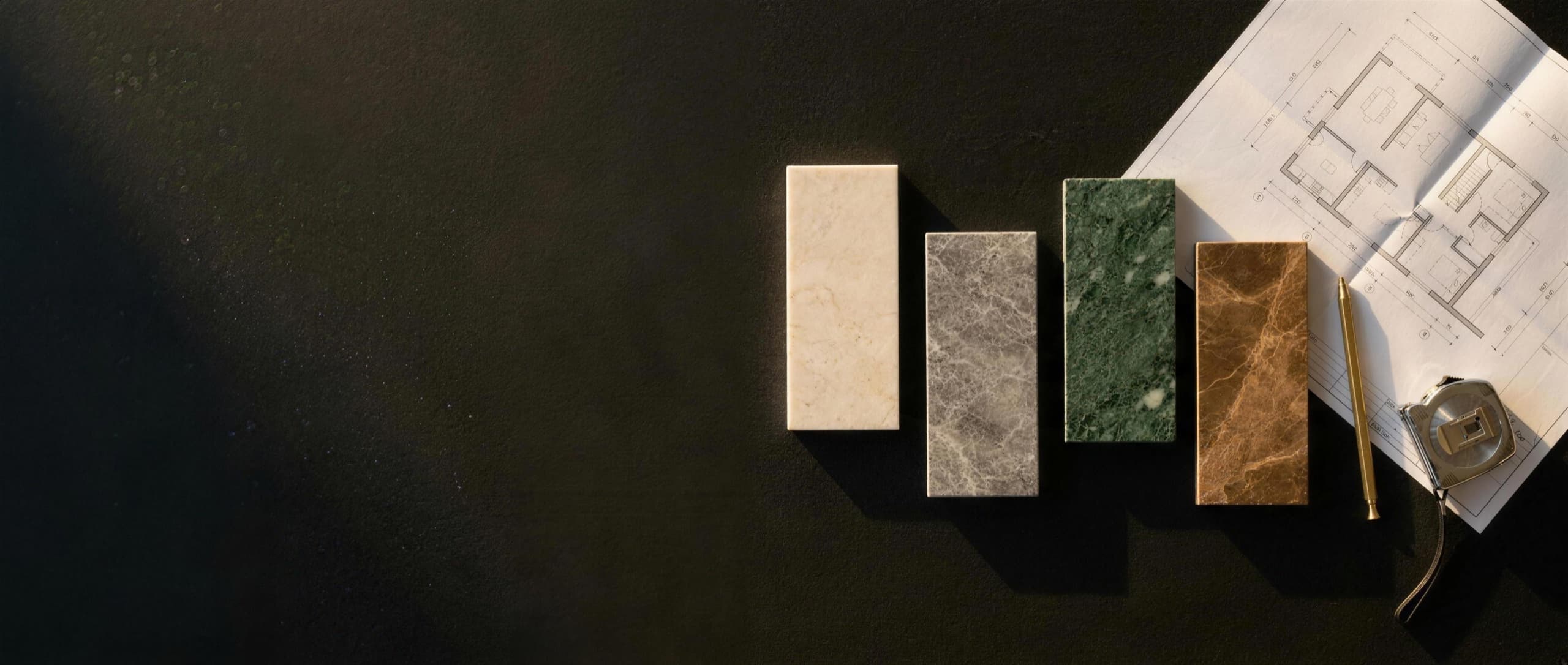 Marble samples laid out beside a floor plan and a pencil on a dark stone table