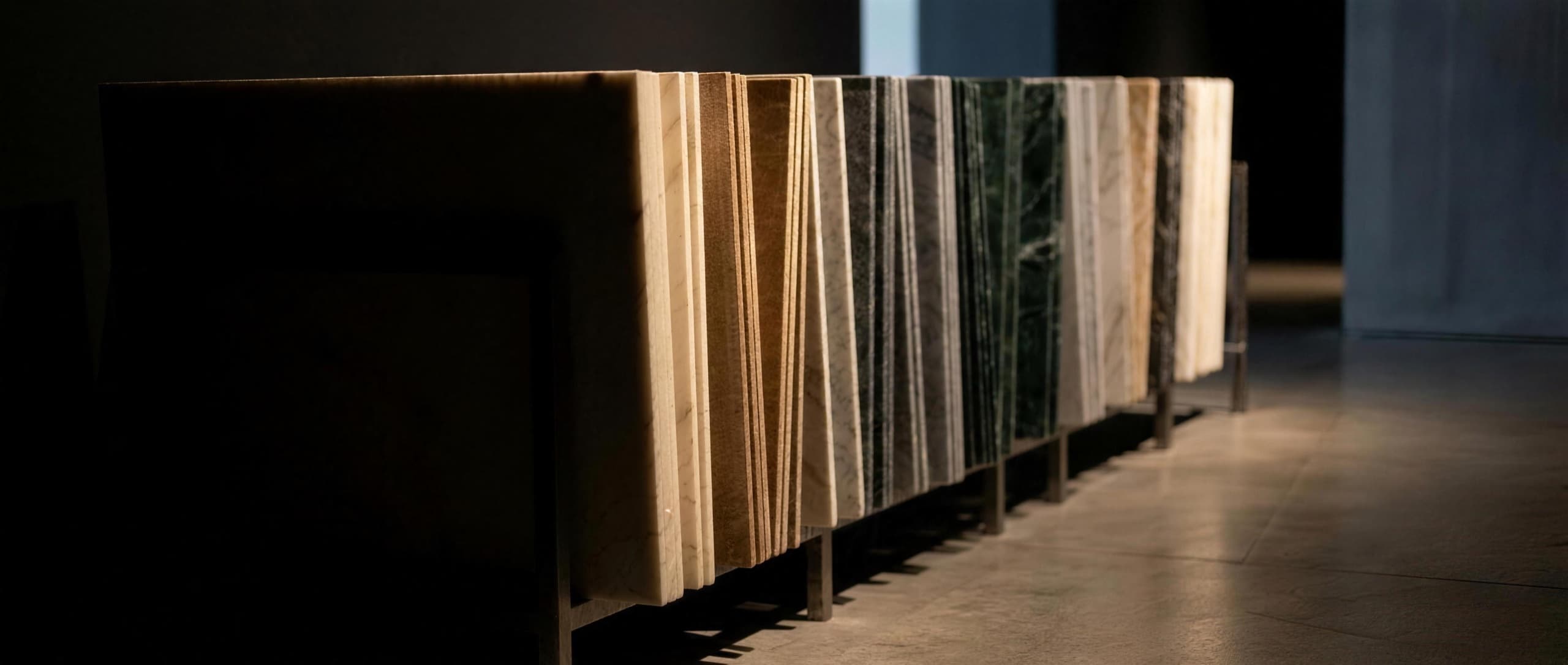 Marble slabs stood on edge in a gallery rack, their polished edges catching warm light in cream, bronze, grey, green and white